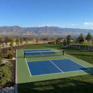 Completed concrete pickleball court with green and blue acrylic coating and white lines in Bluffdale Utah large backyard with Oquirrh Mountain views
